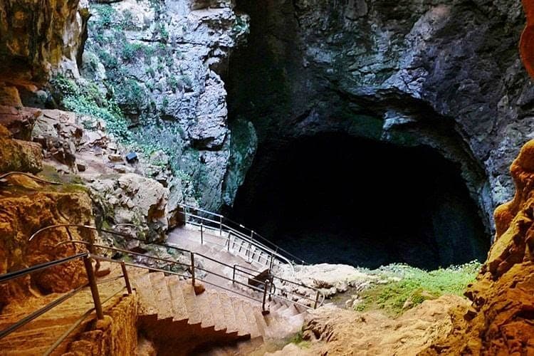 في قاع فتحة الهوة، ممر بدرابزين يؤدي إلى المدخل المظلم للمغارة